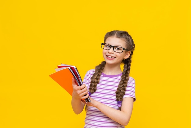 The girl shows her notebooks and rejoices a child on a yellow background A little girl with glasses