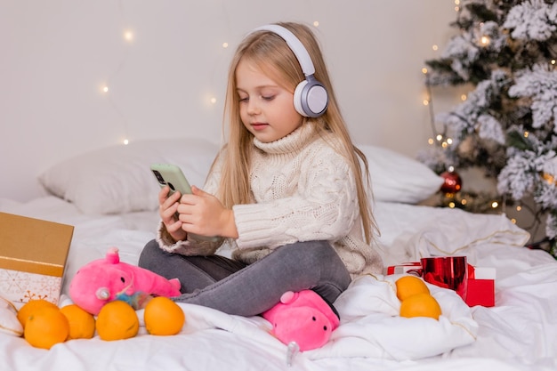 A girl sits on a bed with a christmas tree in the background.