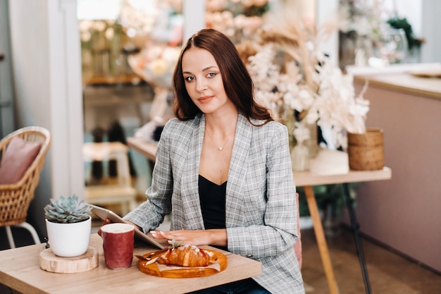 A girl sits in a cafe and looks at a tablet, a Girl in a coffee shop smiles, Distant work.