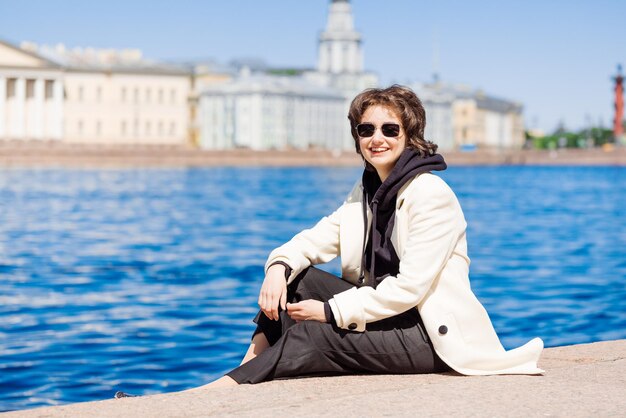 Girl sits on concrete flooring embankment in white coat and black sweatshirt