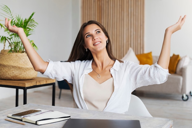 Girl sits at desk in home office and shows joyful gesture with her hands.