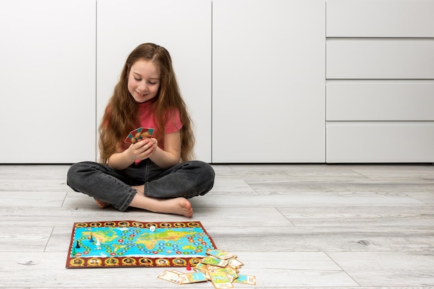 Girl sits on the floor at home holds playing cards in her hands a board game is laid out on the floor