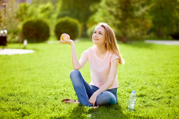 The girl sits on the grass and eat an apple