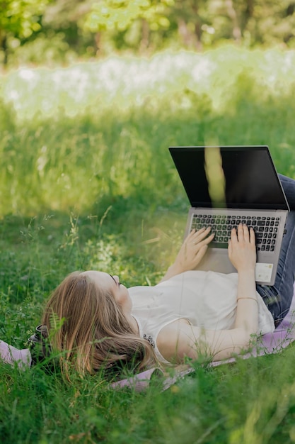 The girl sits on the grass and uses a laptop Education lifestyle technology concept outdoor learning concept