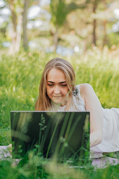 The girl sits on the grass and uses a laptop Education lifestyle technology concept outdoor learning concept