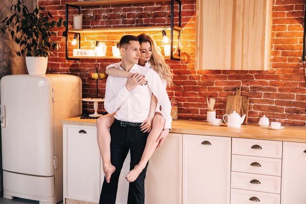 Photo the girl sits and hugs the guy on the back side in a stylish and modern kitchen. loving young couple spending time together at home.