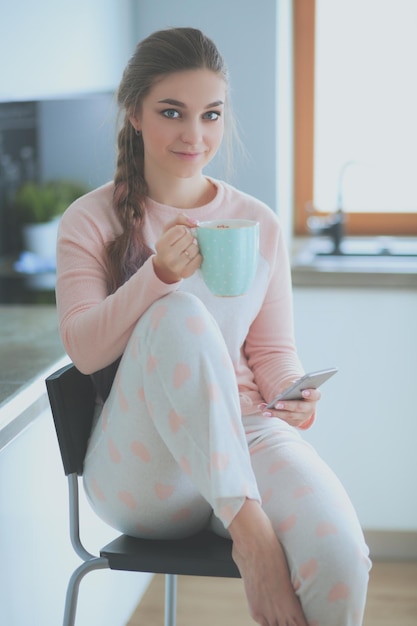 A girl sits on a kitchen counter holding a cup of coffee and a mug of coffee.