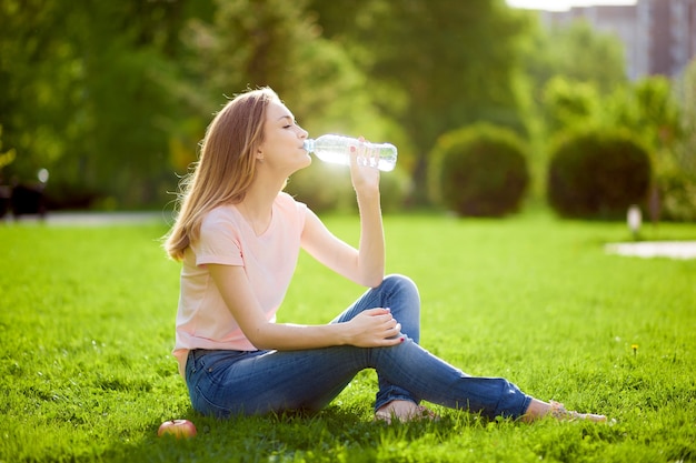 Girl sits on the lawn and drinks water