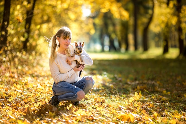 Girl sits and relax on the ground in the autumn forest and plays with Yorkshire Terrier small dog