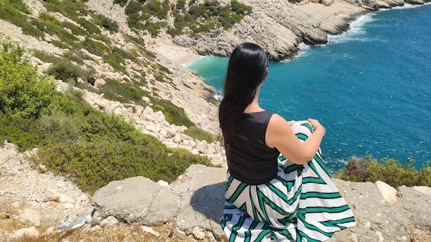 The girl sits on a rock overlooking the blue sea