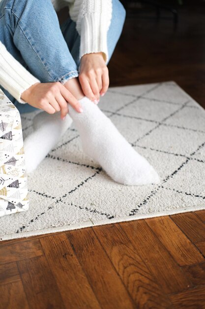 The girl sits on the rug and puts on white fluffy socks