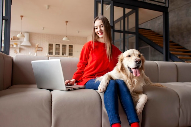 Girl sits on sofa with dog and uses laptop at home woman with golden retriever looks at the computer