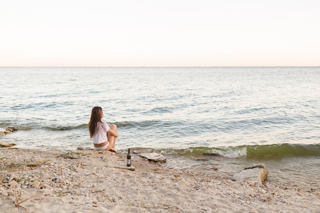 Girl sitting on the beach with a bottle of wine