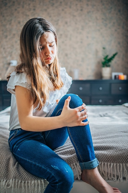 Girl sitting on bed clutching a sore knee.