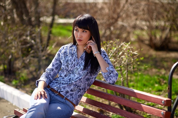  girl sitting on bench in park and talking on phone.