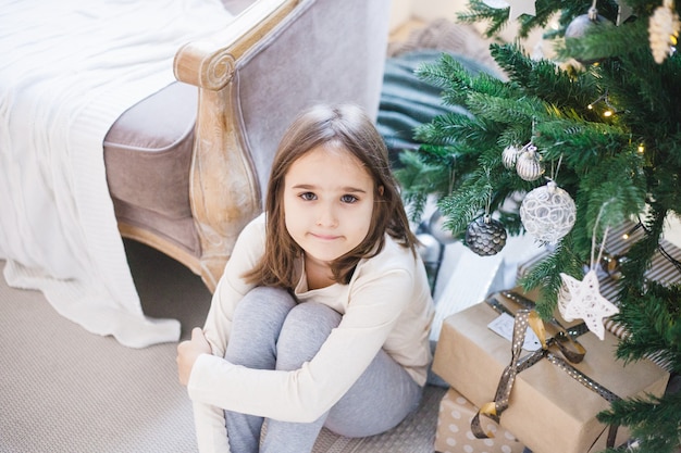 Girl sitting next to Christmas tree at home