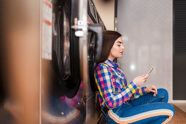 Girl sitting on the floor in a launderette and listening to music on headphones