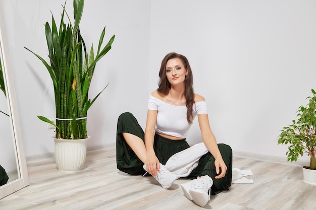 Girl sitting on the floor near a green plant in stylish clothes