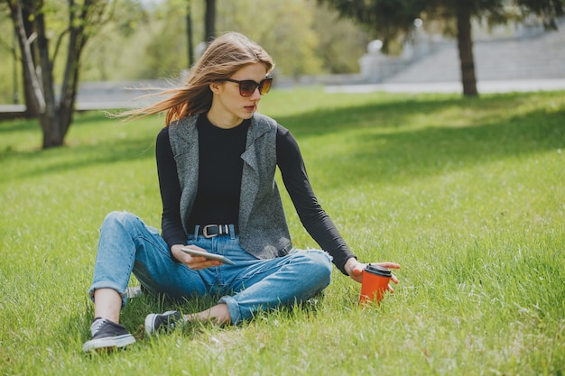 Girl sitting on the grass with coffee and tablet on the street.