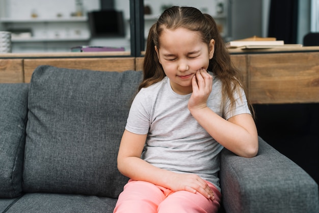 Girl sitting on gray sofa suffering from toothache