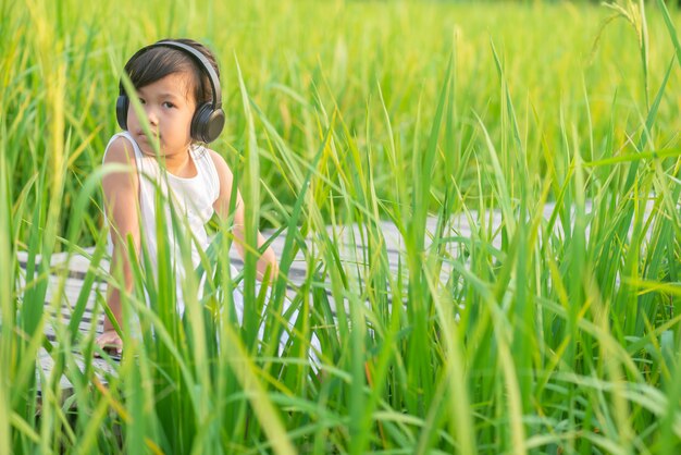 girl sitting and listening to music on wooden bridge in rice field on sunset