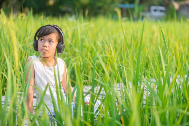 girl sitting and listening to music on wooden bridge in rice field on sunset 