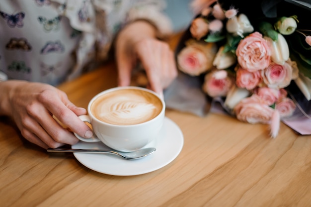 Girl sitting at the table holding a cup of coffee near the beautiful bouquet