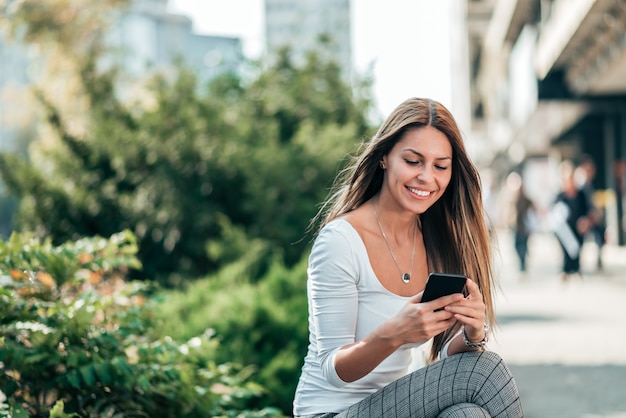 Girl sitting in a town street using smartphone.