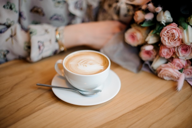 Girl sitting at the wooden table with a cup of coffee and beautiful bouquet