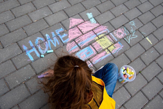 A girl of six years old draws a house on the asphalt with crayons The concept of coziness Childhood