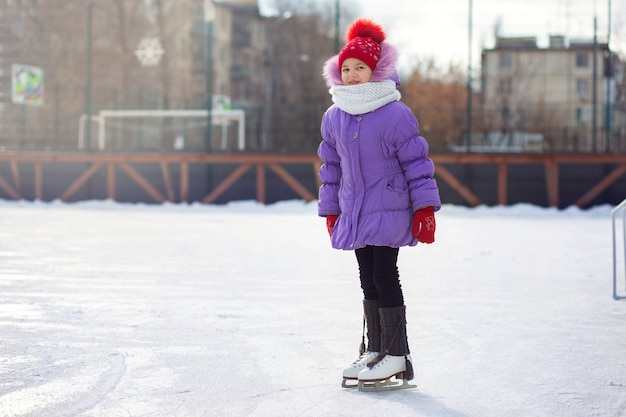 A girl skates on an ice rink in winter. Skating rink in the courtyard in the city. Child learns to skate