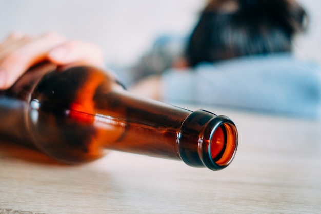 Girl sleeping on a table with a bottle of beer.