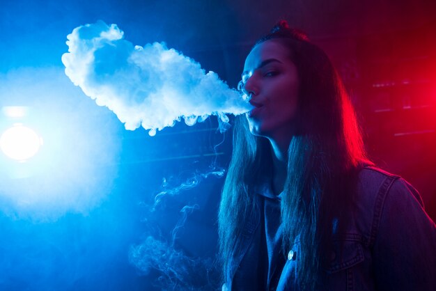 Photo girl smokes a cigarette and lets out smoke in a nightclub.