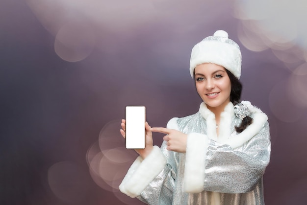 Girl in a snow maiden costume, holding a smartphone in her hand and showing on the phone screen