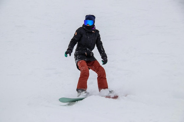 A girl on a snowboard rides down the side of the mountain