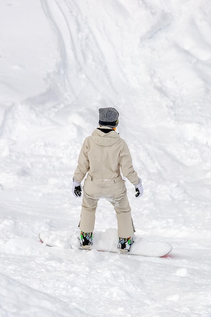 Girl snowboarding from the mountainside view from the back