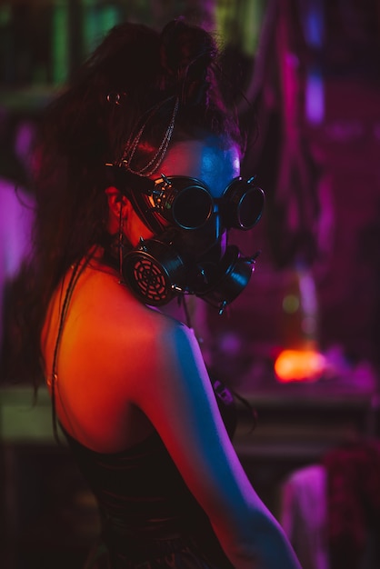 Girl soldier in cyberpunk style with a gas mask and glasses with neon lighting in the garage. Steampunk style in a post-apocalyptic world