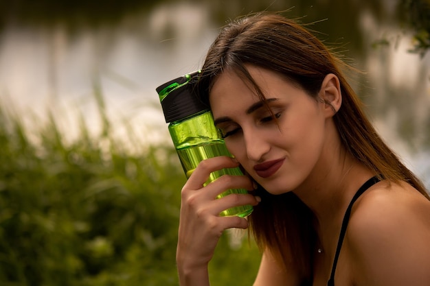 A girl in a sports uniform holds a sports bottle in her hands is dressed in a black sports top