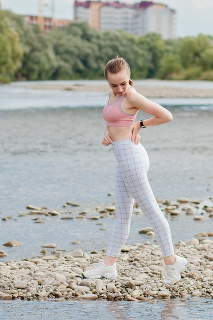 Girl in sports uniforms makes a stretch on the river bank