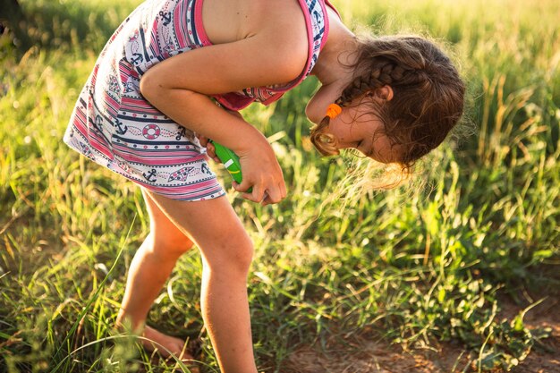 Girl sprays mosquito spray on the skin in nature that bite her hands and feet. Protection from insect bites, repellent safe for children. Outdoor recreation, against allergies. Summer time