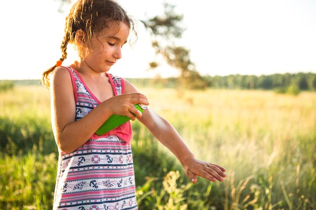 Photo girl sprays mosquito spray on the skin in nature that bite her hands and feet. protection from insect bites, repellent safe for children. outdoor recreation, against allergies. summer time