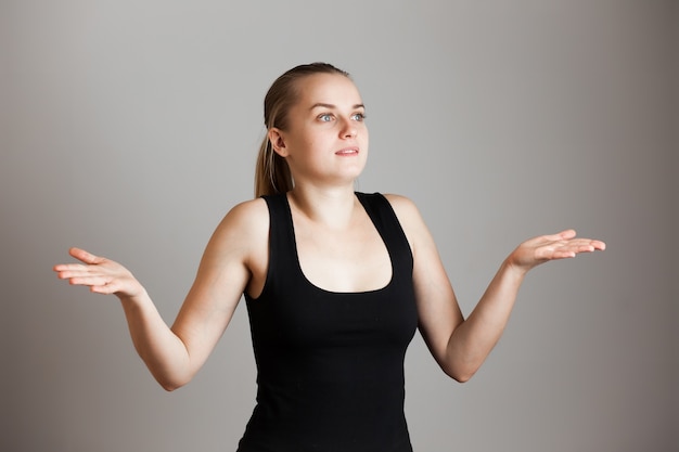 Girl spreading hands with confused and unsure expression  Over grey wall. Copy space.