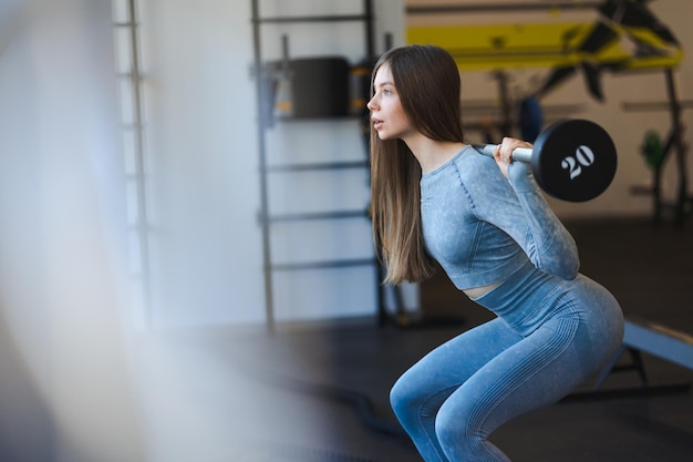 Girl squats with a barbell in the gym Sportswoman doing exercises on the buttocks muscles