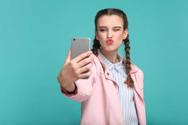 Girl standing holding mobile smart phone and doing selfie or video calling with kiss