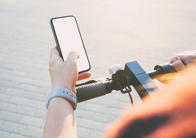 Girl standing with electric scooter and showing the phone with blank white screen