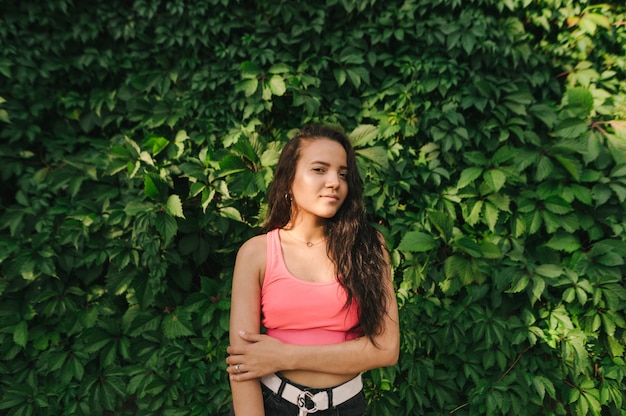 Girl stands against a background of green wall with ivy