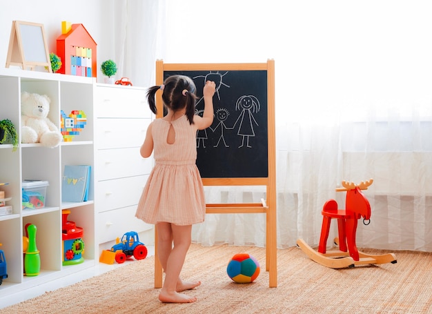 A girl stands in the children's room with a blackboard and draws a family with chalk