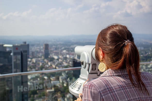 The girl stands on a high tower in the city of Frankfurn on Main and looks at the city