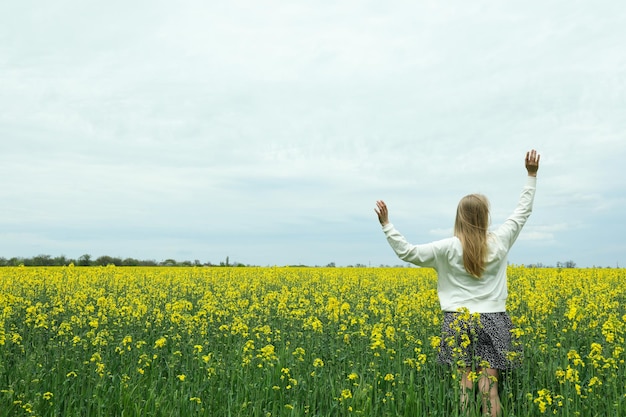 A girl stands in a rapeseed field on a summer day