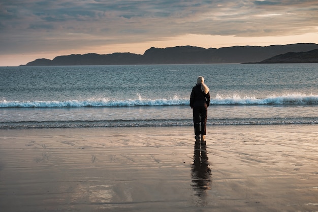 A girl stands on the shore of the Barents Sea at sunrise